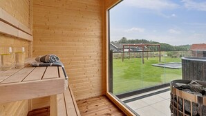 A wooden interior with a bench and a large window overlooking a grassy area and a playground. - Stunning home in Spøttrup with sauna (Spøttrup)