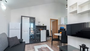 Un espacio habitable compacto con kitchenette, comedor y zona de estar con televisor.
