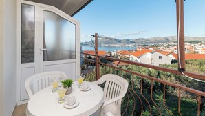 Un balcón con una mesa dispuesta para dos personas, con vistas a un pueblo costero de casas con tejados rojos y un puente al fondo.