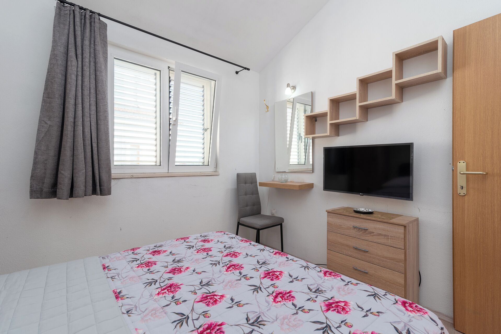 A bedroom with a bed, a chair, a TV, a dresser, and a window with curtains.