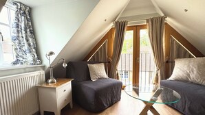 A cozy attic bedroom with a sloped ceiling, a wooden floor, a glass table, and a nightstand with a lamp. - The Garden Rooms, Selborne - Jane Austin country & the South Downs National Park (Selborne)