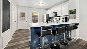 A modern kitchen with a bar area, white cabinets, and a wooden floor.