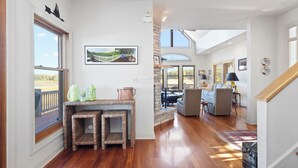 Een ruime woonkamer met houten vloer, een eettafel met rieten stoelen, een bank en uitzicht op een brug door een groot raam.