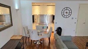 A modern living room with a dining area, a sofa, a coffee table, and a kitchen in the background. - 2 Bed Apartment Central London Canary Wharf (London)