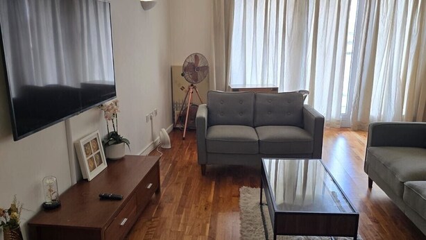Un soggiorno con televisore a schermo piatto, un divano grigio, un tavolino da caffè e un mobiletto in legno.