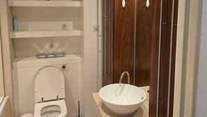 A modern bathroom with a toilet, sink, and wooden cabinet. - 2 Bed Apartment Central London Canary Wharf (London)