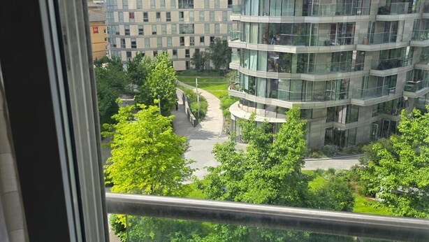 A view of a modern apartment building with multiple floors and balconies, surrounded by greenery and a parking area. - 2 Bed Apartment Central London Canary Wharf (London)