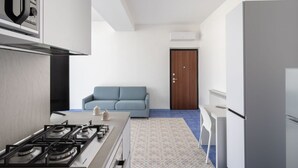 Een moderne keuken met een gasfornuis, een koelkast en een blauwe bank in de woonruimte.