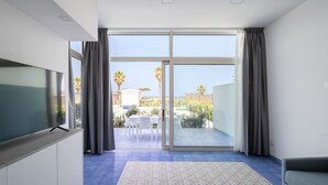 Een moderne kamer met een grote schuifglazen deur die leidt naar een terras, een flatscreen televisie bevestigd aan een kast, en een kamerbreed tapijt op de vloer.