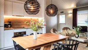 A modern kitchen with a wooden table and chairs, a coffee machine, and a vase with flowers. There are two hanging pendant lights and a sofa in the living area. - Stunning home in Somme-Leuze with WiFi (Somme-Leuze)