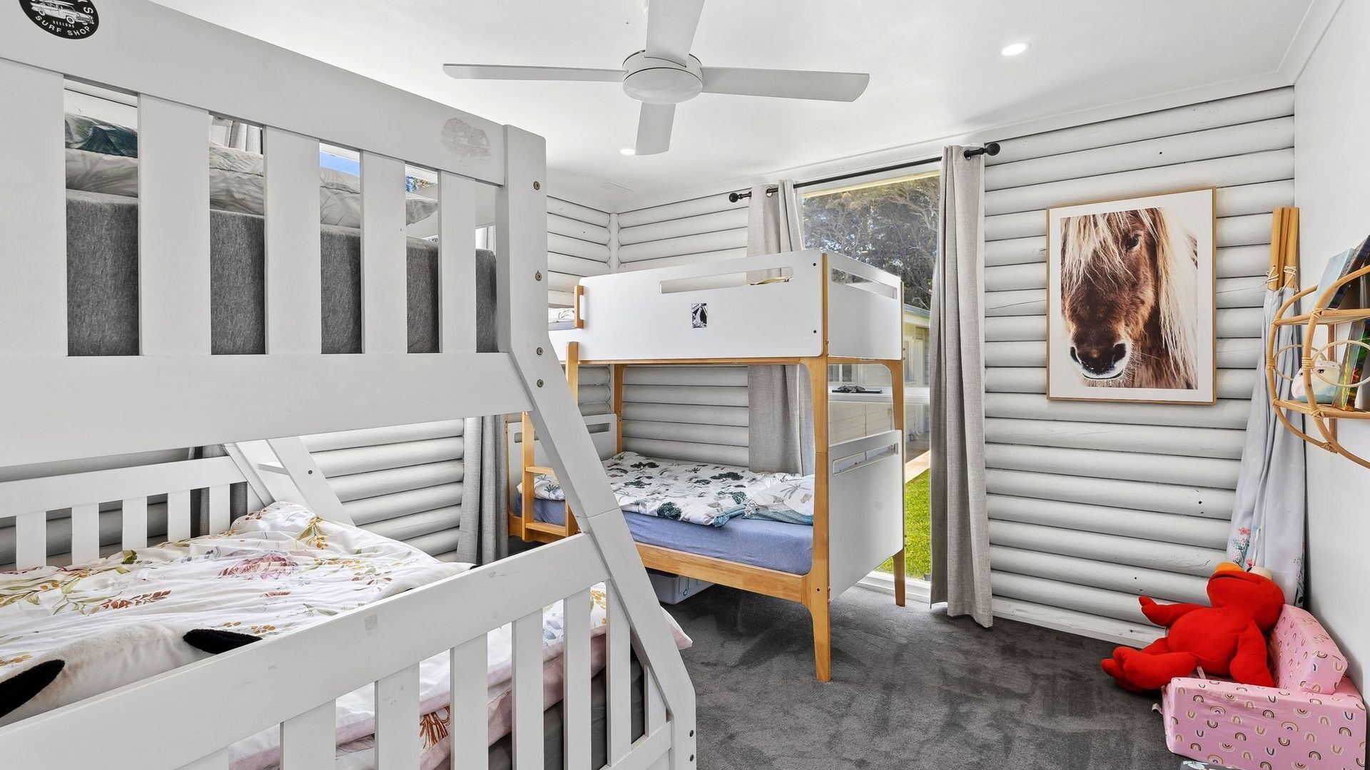 A child's bunk bed room with a ceiling fan, a window, and a framed picture on the wall.