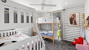 A child's bunk bed room with a ceiling fan, a window, and a framed picture on the wall.