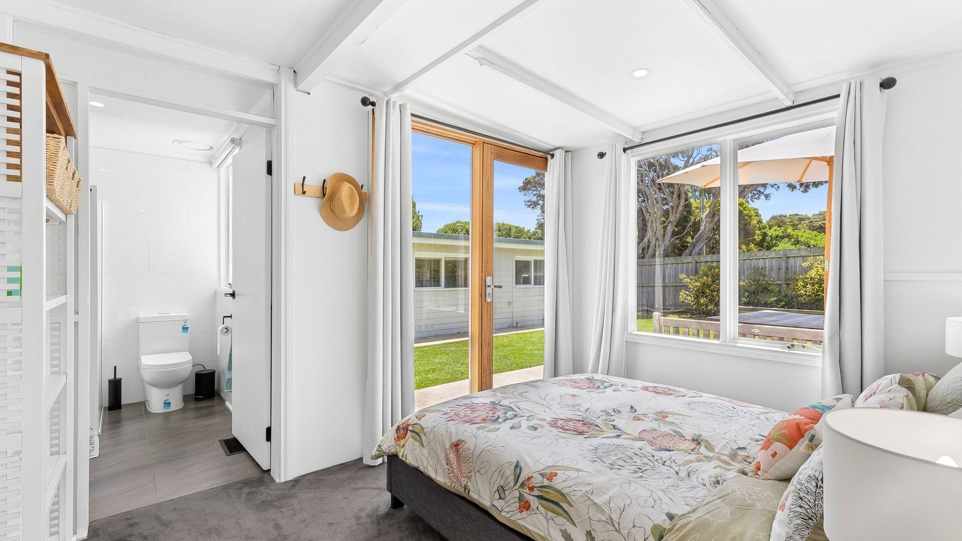 A bedroom with a bed, a window with curtains, a door leading to a bathroom, and a view of the outside.