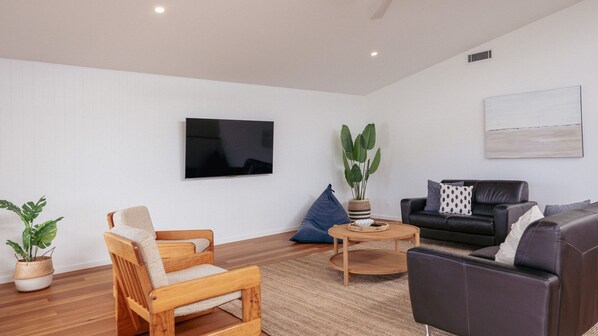 A modern living room with a flat-screen TV, a coffee table, a sofa, and two chairs.