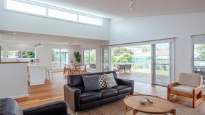 A spacious living area with a black leather sofa, a wooden coffee table, and a dining area with a table and chairs. - Seaglass Beach House - Beautifully designed retreat in the heart of Narrawallee (Narrawallee)