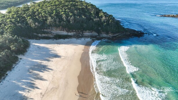 An aerial view of a beach with clear turquoise waters, a sandy shore, and a forested island. - Seaglass Beach House - Beautifully designed retreat in the heart of Narrawallee (Narrawallee)