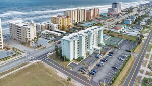 An aerial view of a coastal hotel with multiple buildings, parking lots, and a beach in the background.
