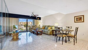 A spacious living room with a balcony, a dining area, and a ceiling fan.
