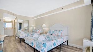 Een hotelkamer met twee bedden, een klein bureau, een spiegel en een badkamer die door een open deur zichtbaar is.