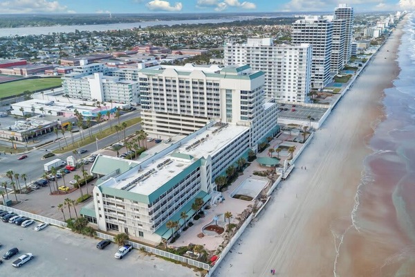 Aerial view of beachfront condominiums along a wide sandy shore with ocean waves.