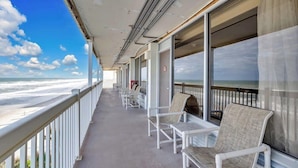 Een balkon met witte stoelen en uitzicht op het strand.