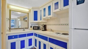 A kitchen with white cabinets and blue accents, a microwave, coffee maker, and a refrigerator. - Beachfront studio w/ direct Atlantic views (Daytona Beach)