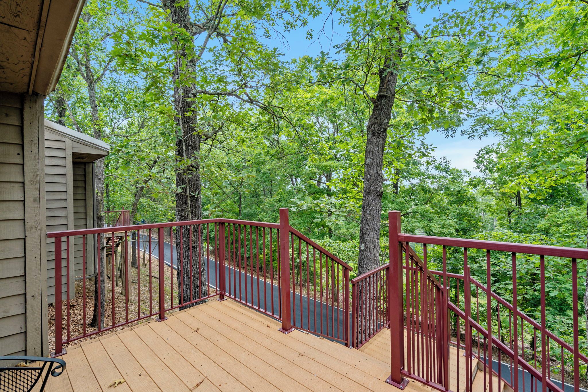 A wooden deck with a red railing overlooking a forested area.
