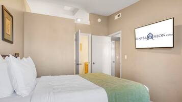A hotel room with a bed, a green throw, a framed picture, and a sign on the wall.