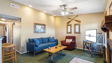 A living room with a blue sofa, a wooden coffee table, a red armchair, and a ceiling fan.