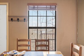 A room with a table, two chairs, a window with blinds, and a coat rack with hooks.