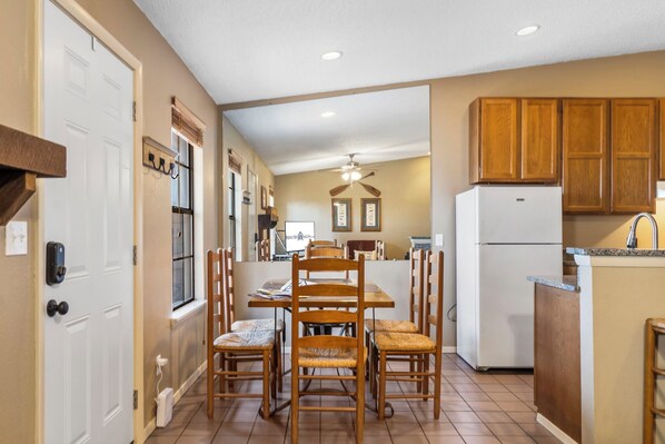 A kitchen with wooden cabinets, a refrigerator, and a dining area with chairs and a table.