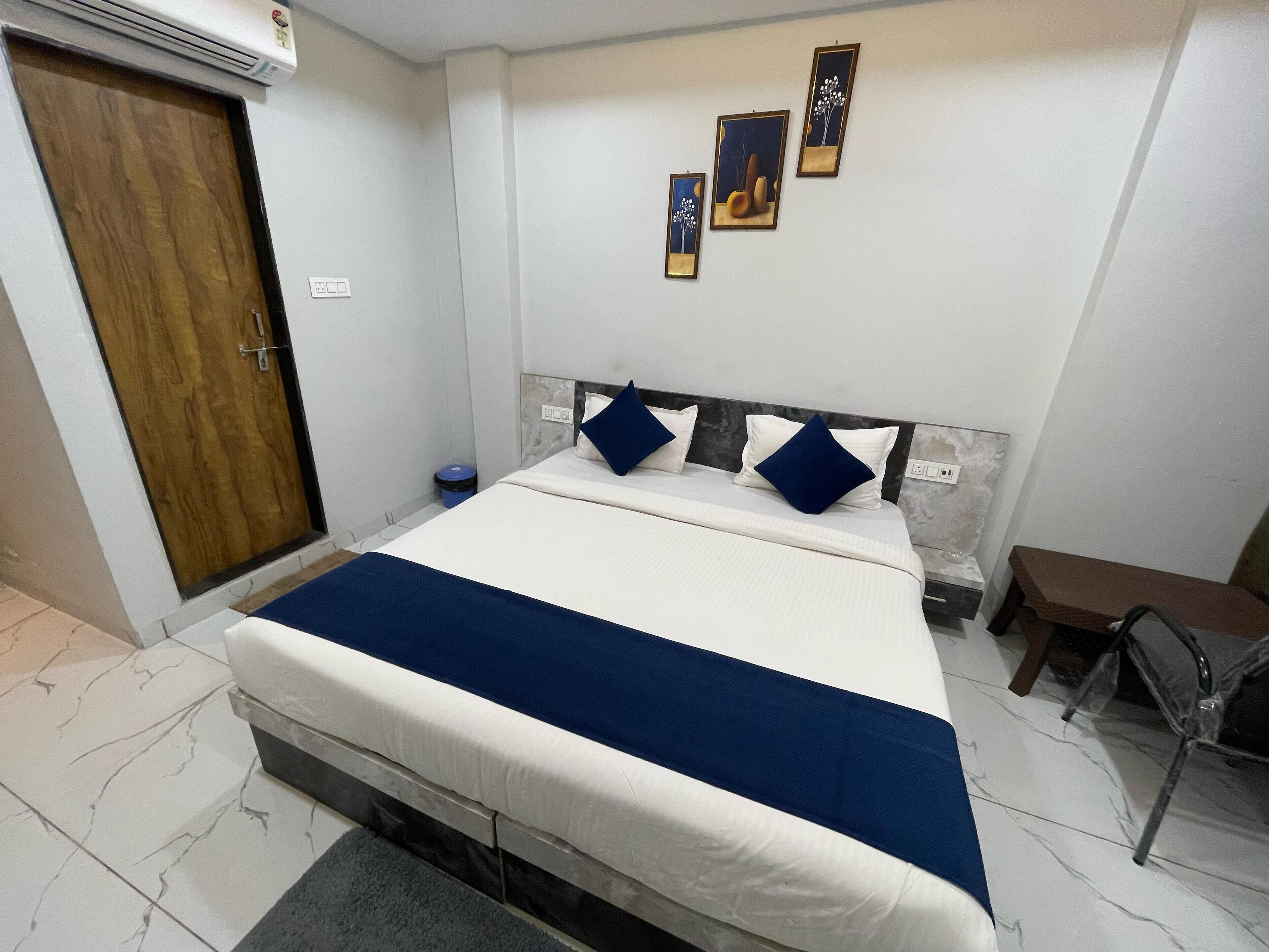 Quarto com uma cama, porta de madeira, lixeira azul e três obras de arte penduradas na parede.