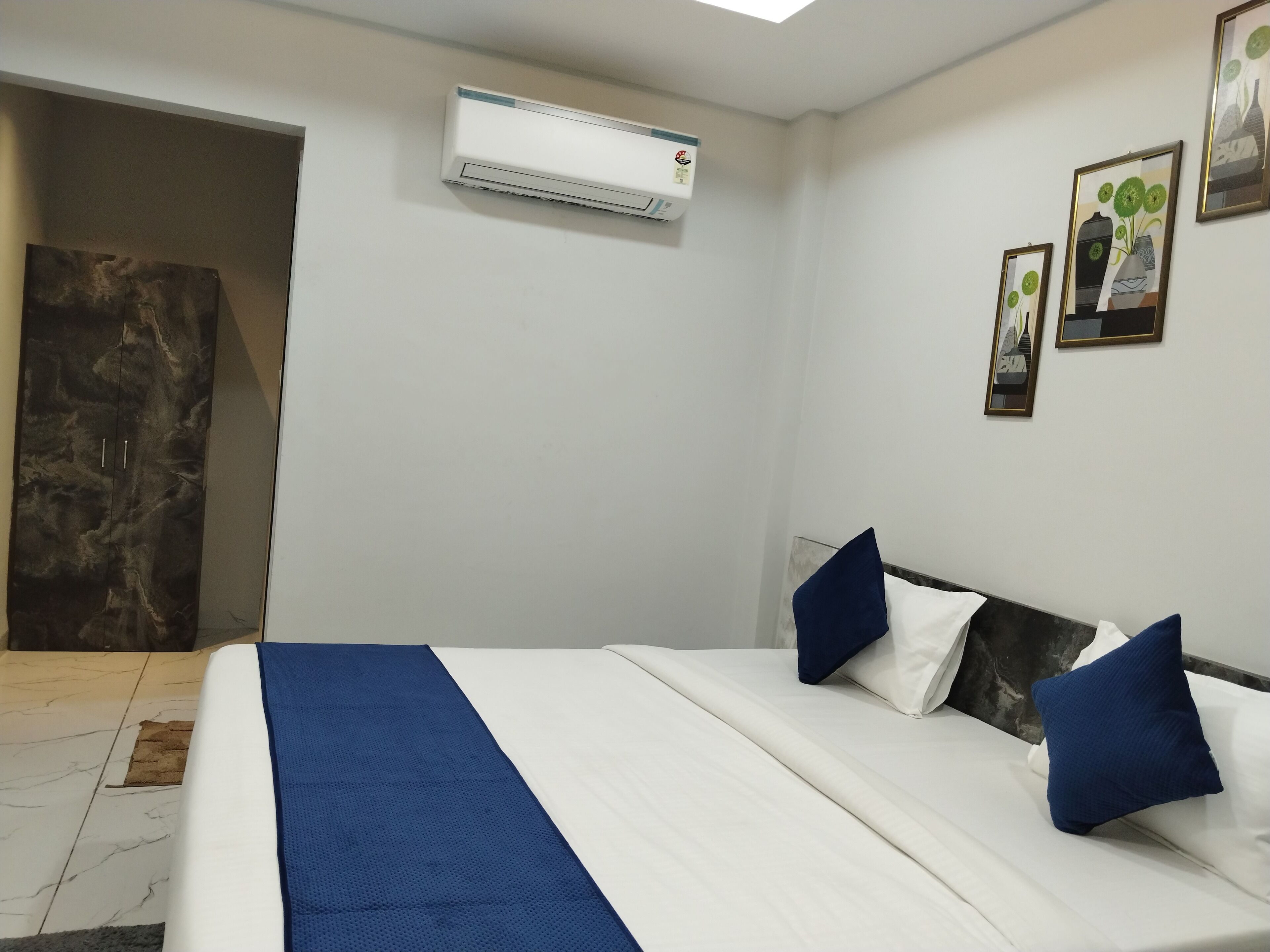 A bedroom with a bed, pillows, an air conditioning unit, and a door leading to another room.