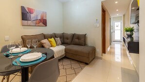 A modern living room with a sectional sofa, a dining table set with plates and glasses, and a ceiling fan. - Cosy in Copacabana 7 minutes from the beach | FM211 (Rio de Janeiro)