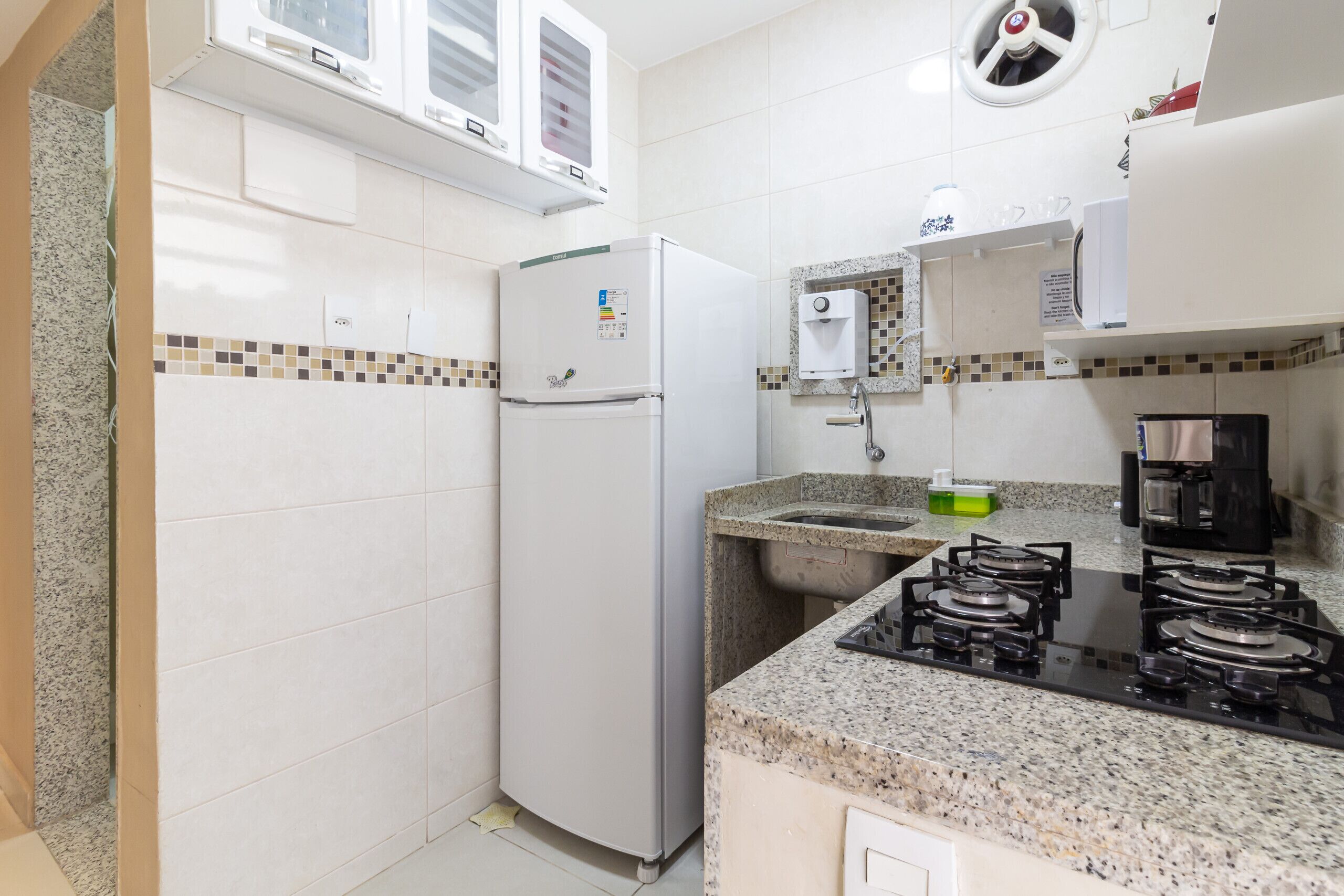 Una cocina compacta con refrigerador, estufa, lavaplatos y salpicadero de azulejos.