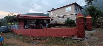 A two-story house with a red brick exterior, a balcony, and a small garden area.