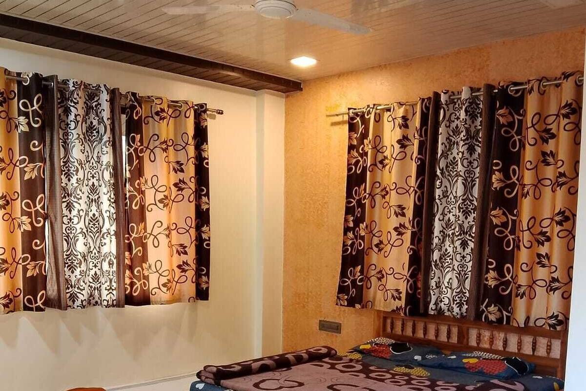 Ein Schlafzimmer mit einem hölzernen Bett, einem kleinen Nachttisch und Vorhängen mit Blättermuster.