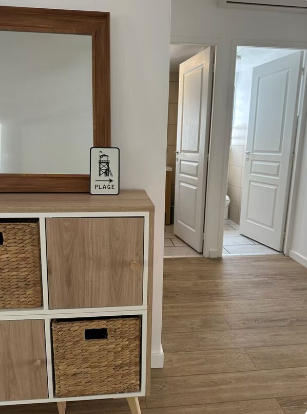 A hallway with a wooden floor, a white cabinet with woven baskets, and a mirror with a 'PLACE' sign. - Little Turtle (Saint-Paul)