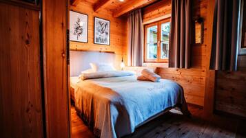 Ein Schlafzimmer einer Holzhütte mit Bett, einem Fenster mit Vorhängen und gerahmten Bildern an der Wand.
