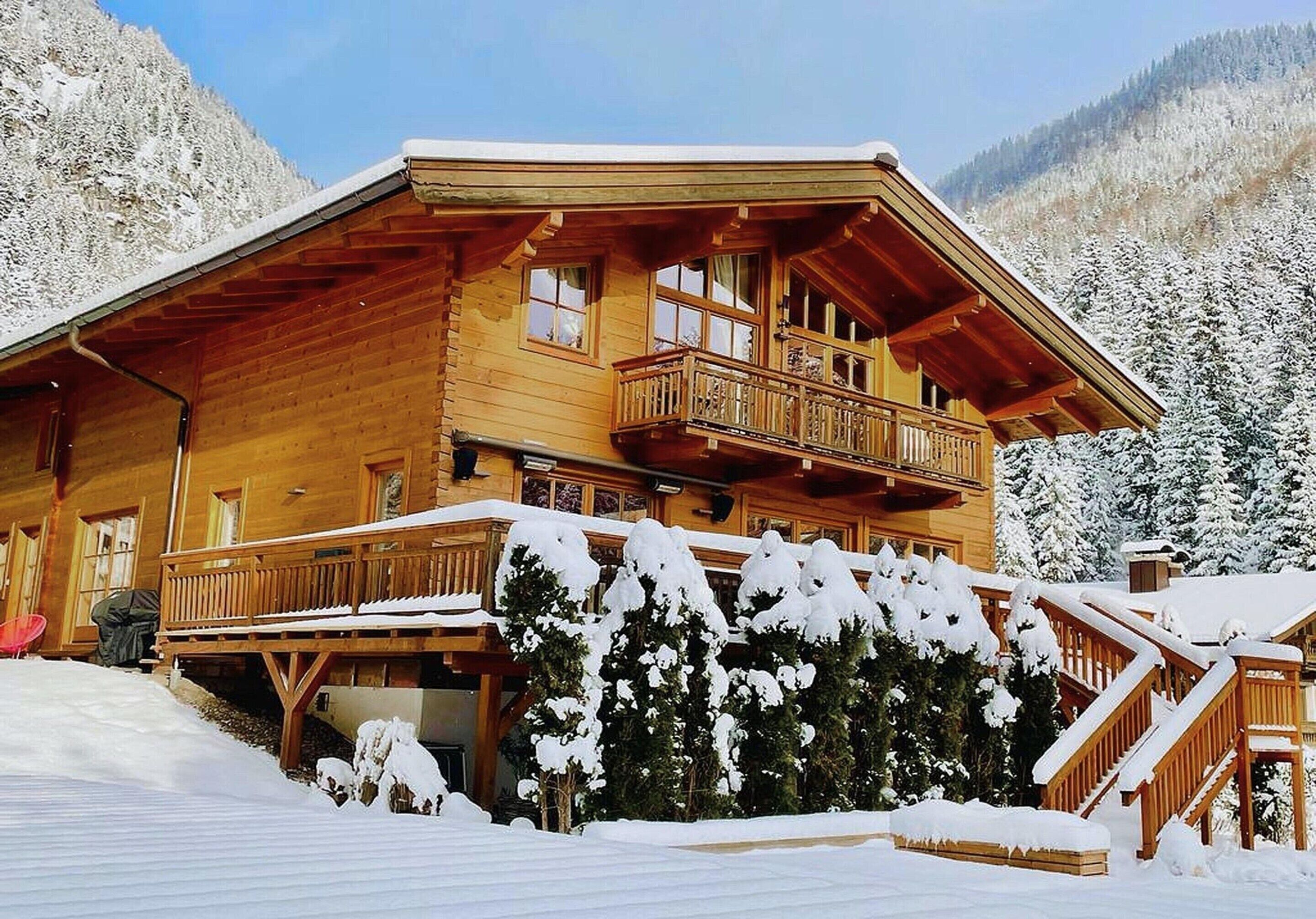 Eine Holzhütte mit Balkon, umgeben von schneebedeckten Bäumen und Bergen.