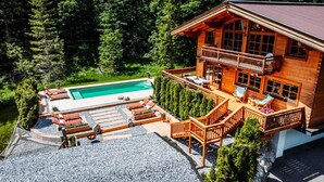 A wooden cabin with a swimming pool, deck chairs, and a balcony overlooking a forested area. - Chalet in Tyrol Near Ski-area (Waidring)