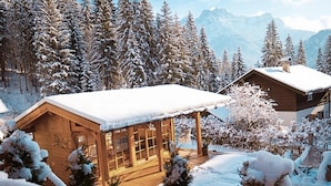 A wooden cabin with a snow-covered roof, surrounded by snow-laden trees and mountains in the background. - Chalet in Tyrol Near Ski-area (Waidring)