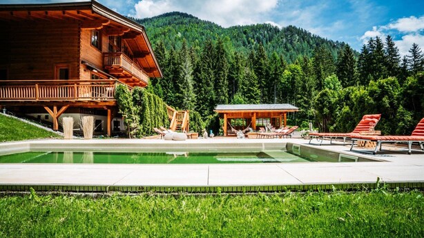 A wooden lodge with a pool, outdoor seating, and a mountainous backdrop. - Chalet in Tyrol Near Ski-area (Waidring)