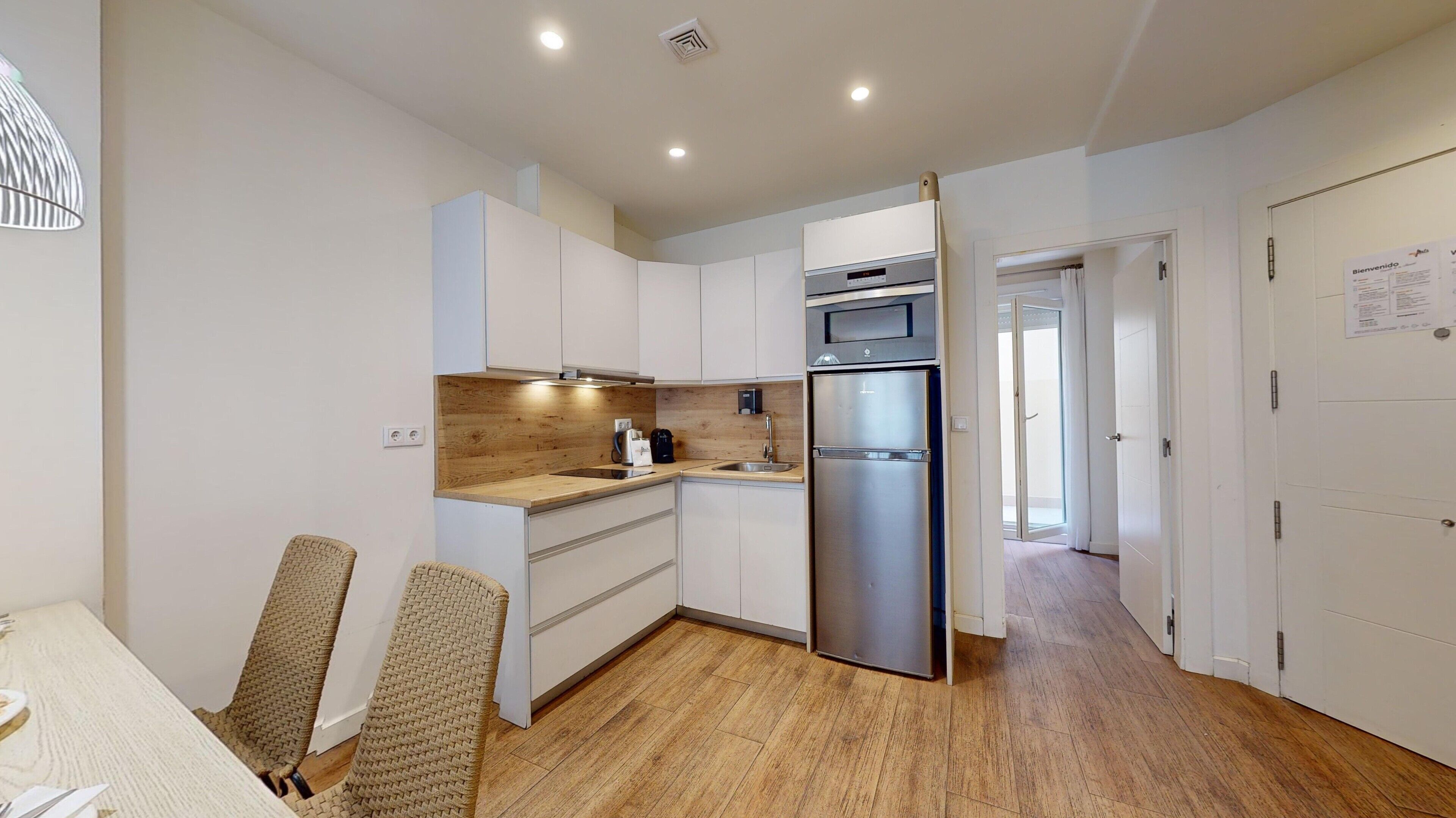 Una cocina moderna con armarios blancos, un refrigerador de acero inoxidable y una encimera de madera.