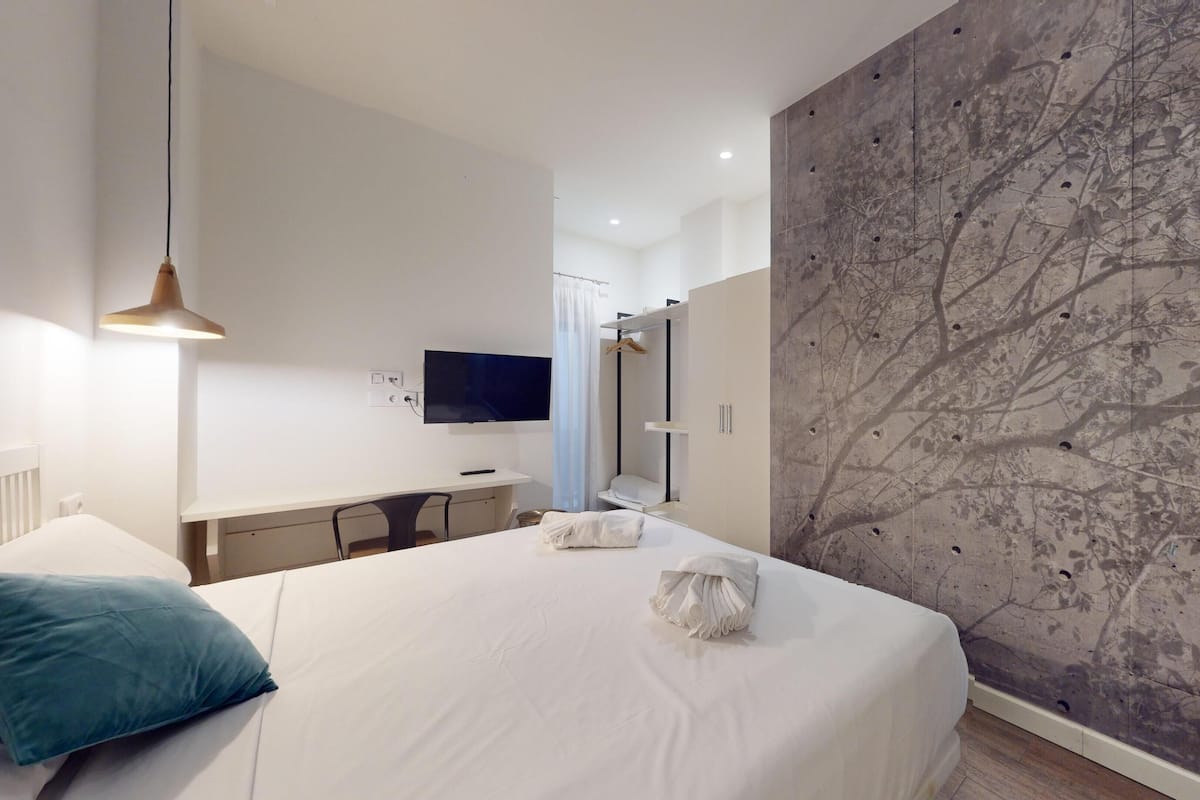 Una habitación de hotel moderna con una cama grande, un escritorio, un televisor de pantalla plana y una pared decorada con un estampado de árboles.