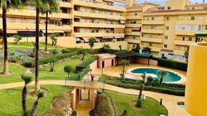 Um hotel com vários andares e um pátio central com piscina, palmeiras e uma pequena ponte.