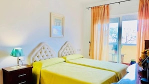Quarto com duas camas, uma mesa de cabeceira, uma luminária e uma janela com cortinas.
