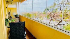 Varanda com cadeira, plantas em vasos e vista para uma rua arborizada.