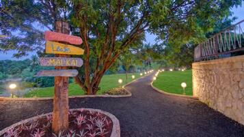 A pathway leading to a sports center and swimming pool, surrounded by lush greenery and a stone wall.