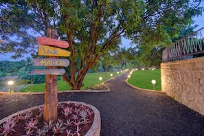 A pathway leading to a sports center and swimming pool, surrounded by lush greenery and a stone wall.